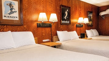 A hotel room with wooden paneling, three beds, wall-mounted lamps, and two posters.