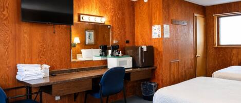 Habitación de hotel con pared de madera, televisor de pantalla plana, escritorio con silla, microondas, refrigerador y dos camas.