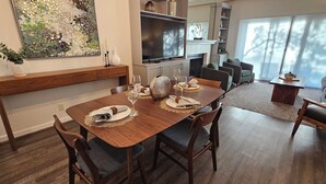 A dining area with a wooden table set for four, a television, and a fireplace. - Modern Condo in Gated Silverado Resort Residential Community (Napa)