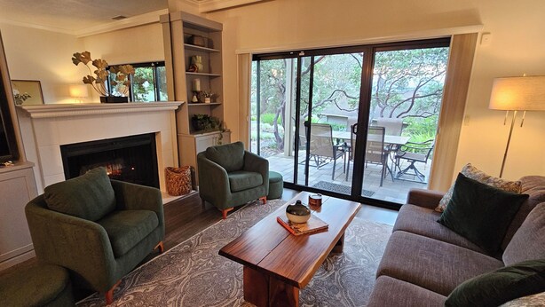 A living room with a fireplace, green armchairs, a sofa, a coffee table, and a view of the outdoors through large sliding glass doors. - Modern Condo in Gated Silverado Resort Residential Community (Napa)