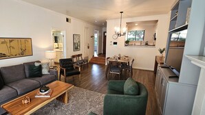 A modern living room with a sofa, coffee table, and chairs. There is a dining area with a table and chairs. The room has a staircase leading to another level. - Modern Condo in Gated Silverado Resort Residential Community (Napa)