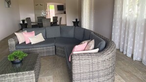 Uma sala de estar moderna com um sofá sectional cinza curvo, uma mesinha lateral com uma planta em vaso, e uma área de jantar ao fundo.