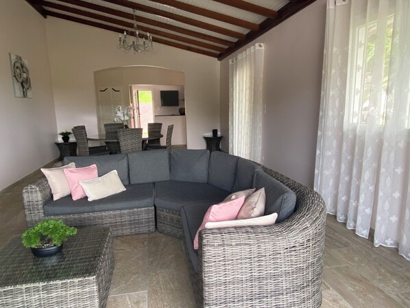 A modern living room with a curved grey sectional sofa, a small side table with a potted plant, and a dining area in the background.
