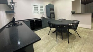 Cozinha moderna com bancada preta, mesa de jantar com quatro cadeiras e forno embutido.