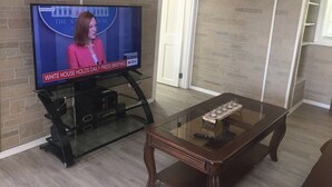 Un saló amb televisió que mostra un informatiu, una taula de centre de vidre i una paret de maó.