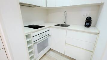 A compact kitchen with white cabinets, a black induction cooktop, a stainless steel sink, and a built-in oven.
