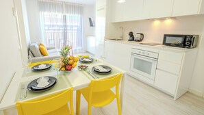 Een moderne keuken met witte kastjes, een magnetron, en een eethoek met gele stoelen en een tafel gedekt voor twee personen.