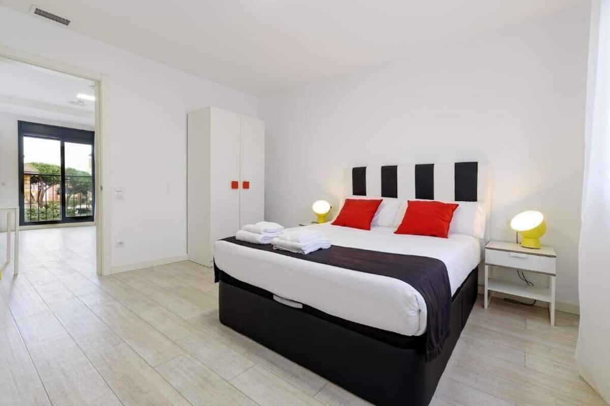 A modern bedroom with a bed, bedside tables, and a view to a balcony.