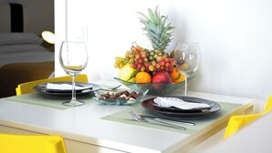 Een hotelkamer met een eettafel gedekt voor twee personen, met een schaal fruit, wijnglazen, borden en bestek.