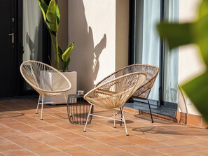Two wicker chairs on a tiled patio with a potted plant and a metal table.