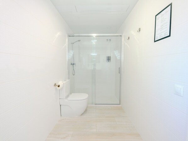 A modern bathroom with a glass-enclosed shower, a toilet, and a framed informational sign on the wall.