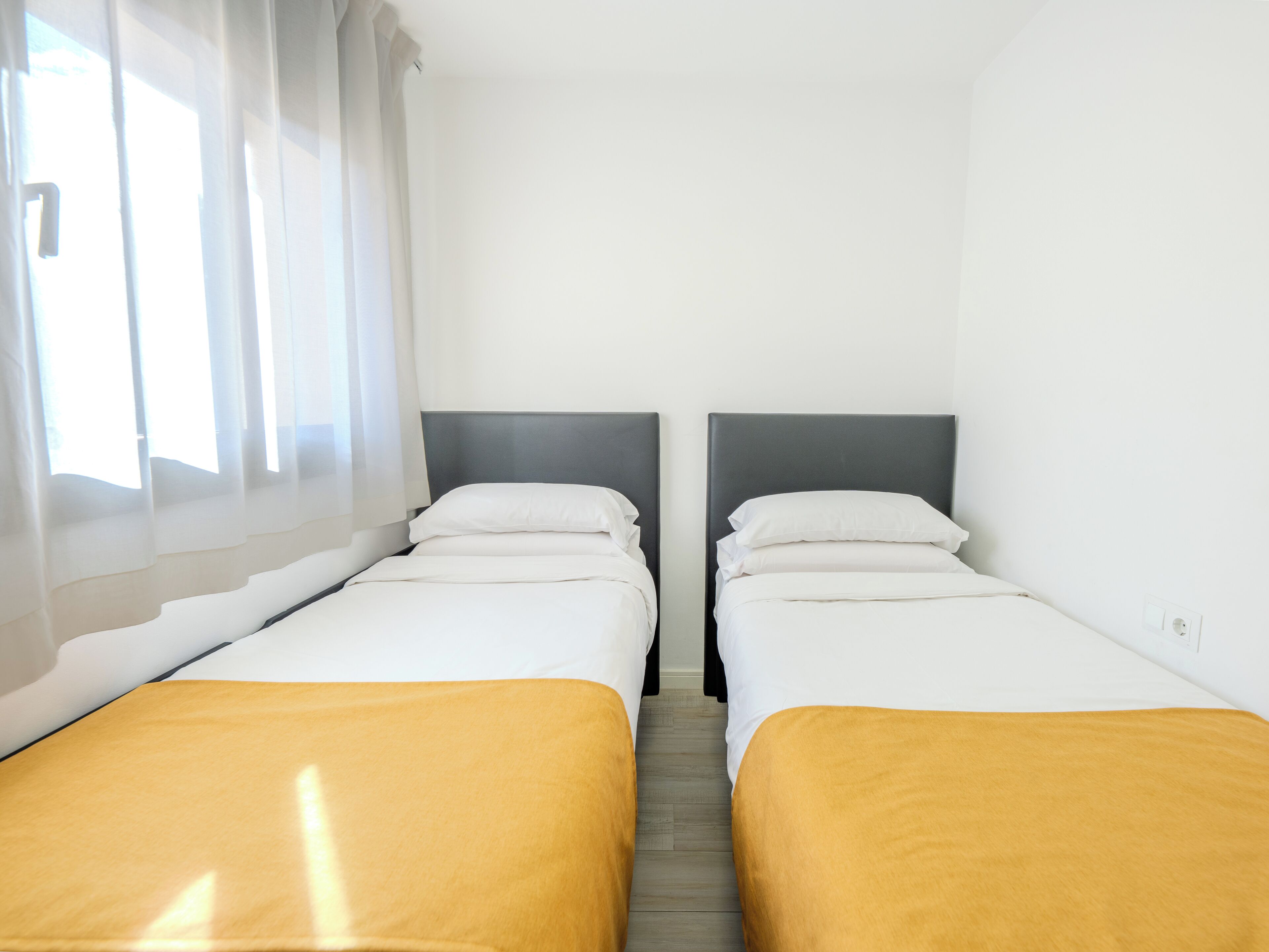 A room with two beds, each with a headboard, and a window with sheer curtains.