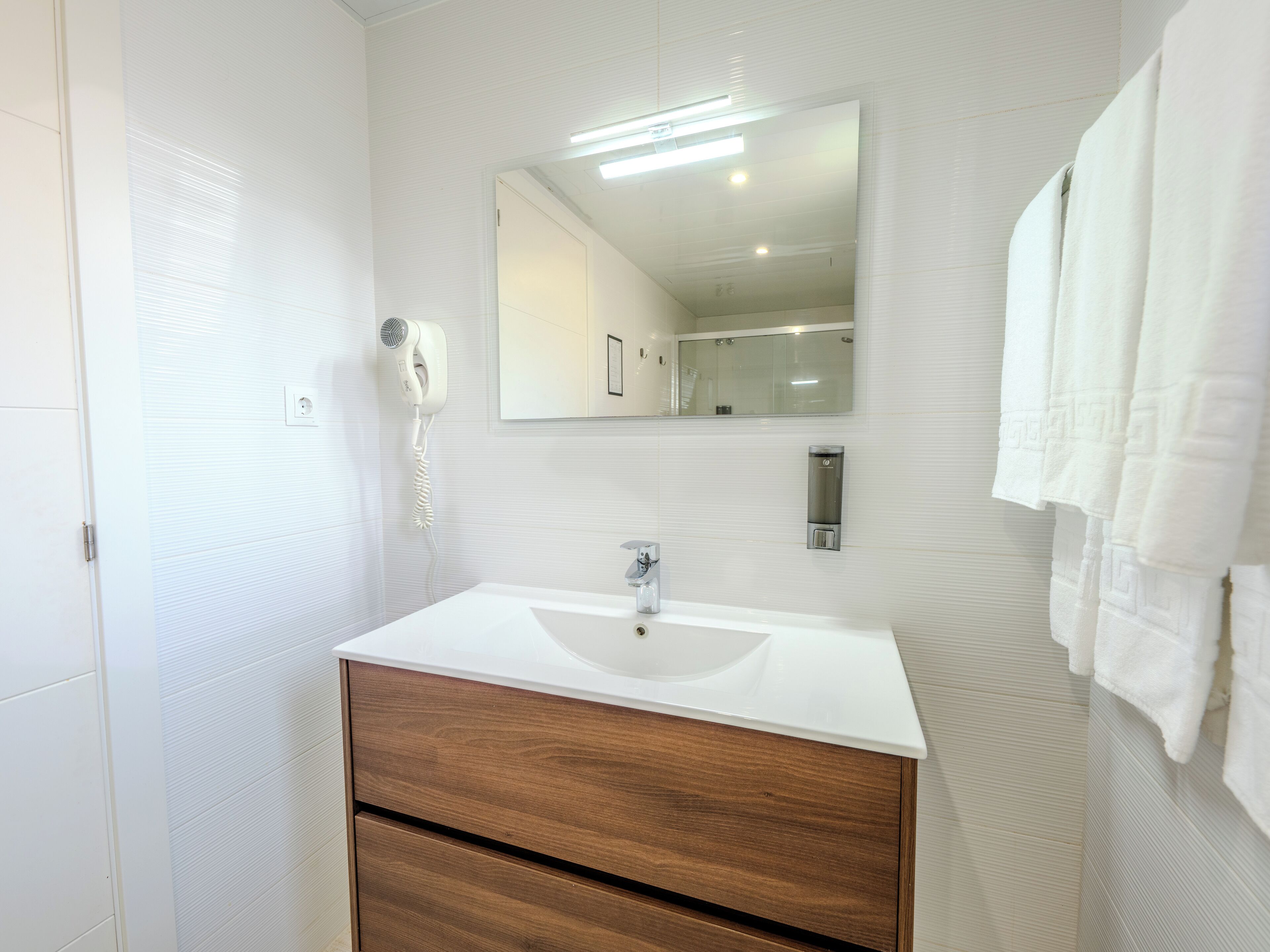 A bathroom with a white sink, wooden vanity, a mirror, a hairdryer, and a towel rack.
