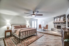 A bedroom with a bed, a ceiling fan, a fireplace, and a stone wall. - Tranquil Acre Oasis, Waterslide Heated Pool, Firepit, Spacious Backyard Estate (Scottsdale)