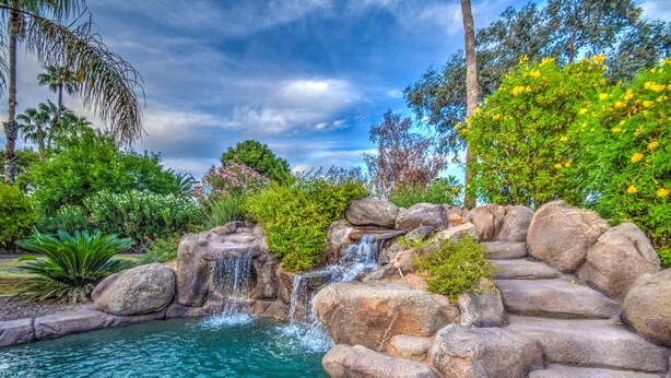A naturalistic garden with a small waterfall, a pool, and lush greenery. - Tranquil Acre Oasis, Waterslide Heated Pool, Firepit, Spacious Backyard Estate (Scottsdale)