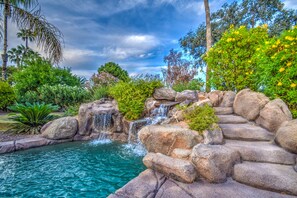 A naturalistic garden with a small waterfall, a pool, and lush greenery. - Tranquil Acre Oasis, Waterslide Heated Pool, Firepit, Spacious Backyard Estate (Scottsdale)