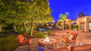 An outdoor patio area with a fire pit, two cushioned chairs, and a pool in the background. - Tranquil Acre Oasis, Waterslide Heated Pool, Firepit, Spacious Backyard Estate (Scottsdale)