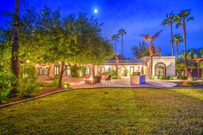 A well-lit outdoor area with a seating arrangement, palm trees, and a building with a tiled roof. - Tranquil Acre Oasis, Waterslide Heated Pool, Firepit, Spacious Backyard Estate (Scottsdale)