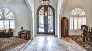 A spacious foyer with a large arched doorway, a wooden bench, a vintage trunk, and a chandelier. - Tranquil Acre Oasis, Waterslide Heated Pool, Firepit, Spacious Backyard Estate (Scottsdale)