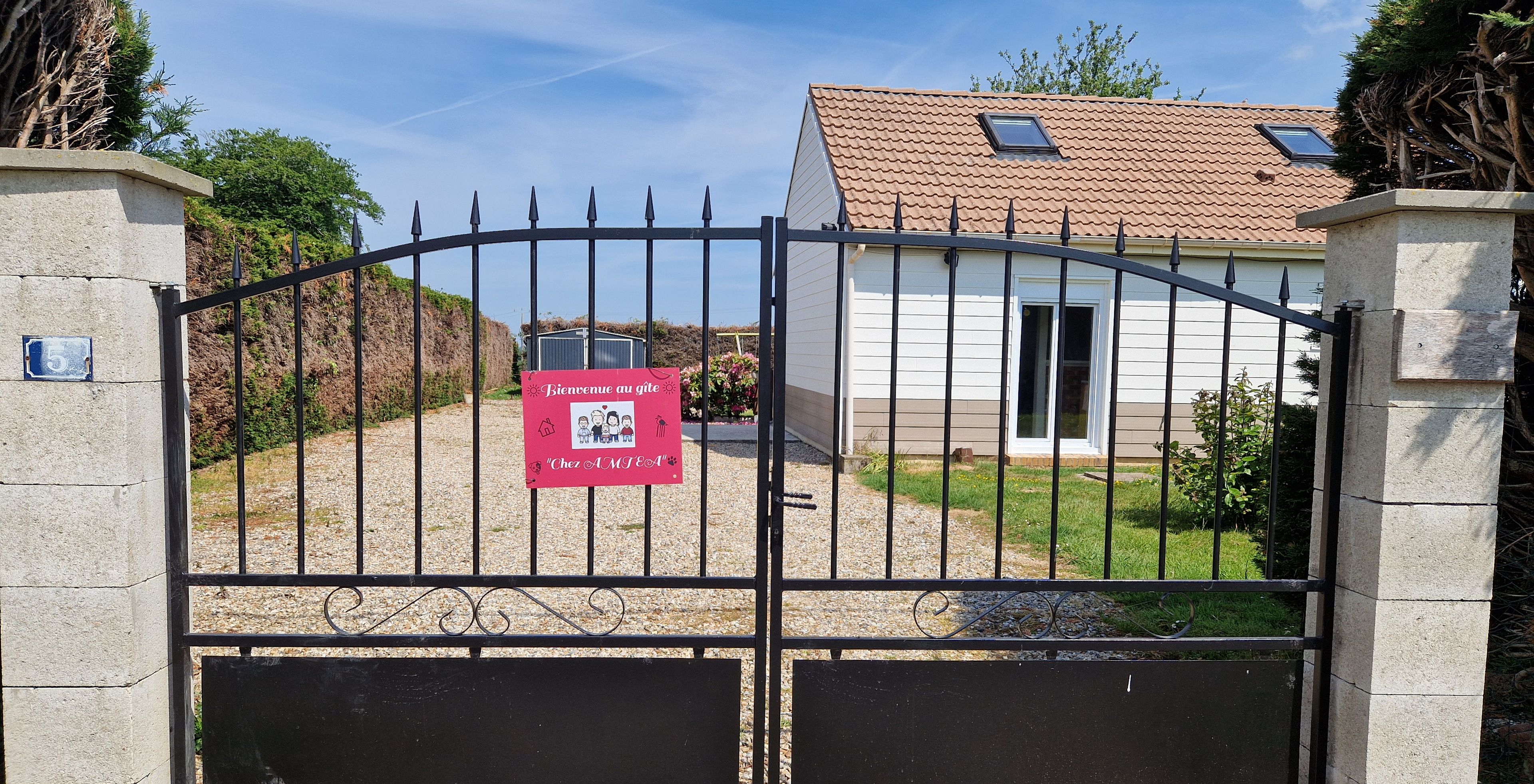 A gated entrance with a welcome sign, a house with a tiled roof, and a gravel driveway.