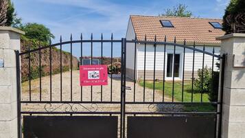 A gated entrance with a welcome sign, a house with a tiled roof, and a gravel driveway.