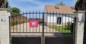 A gated entrance with a welcome sign, a house with a tiled roof, and a gravel driveway.