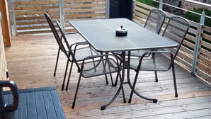Un patio cubierto con una mesa y sillas de metal, un banco y una pequeña caja de almacenamiento negra.