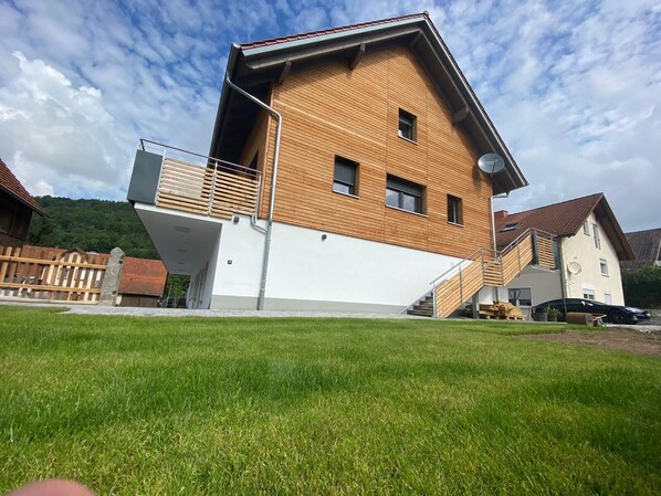 A modern two-story house with a wooden facade, a balcony, and a staircase leading to the upper floor.
