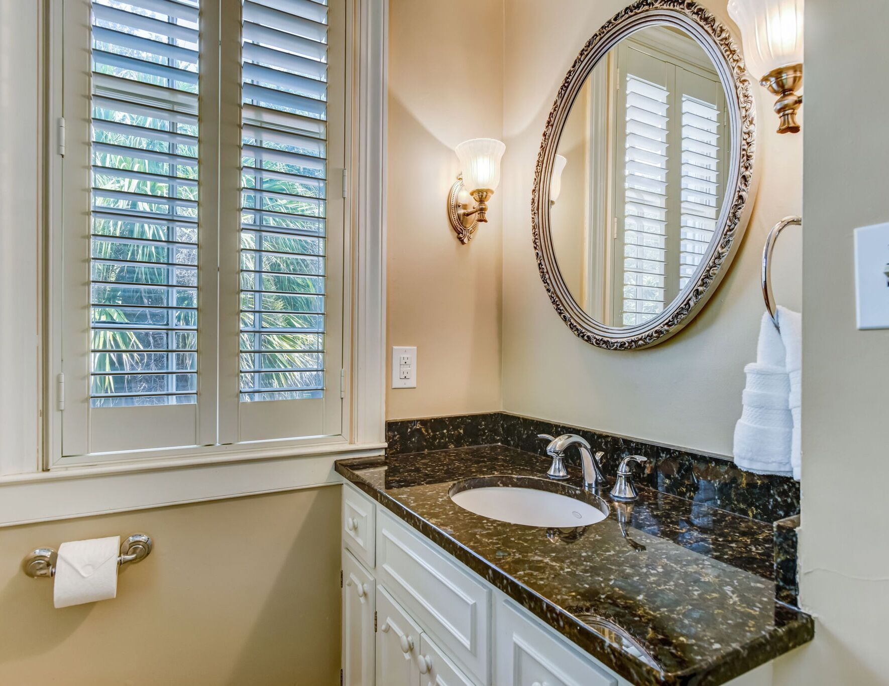 A bathroom with a marble sink, a large mirror, and a window with blinds.