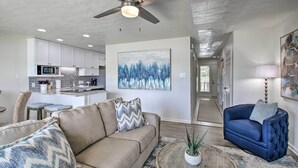 A modern living room with a beige sofa, a blue armchair, and a coffee table. A kitchen is visible in the background with white cabinets and a microwave. - Balcony & Lake Access: Hot Springs Getaway! (Hot Springs)