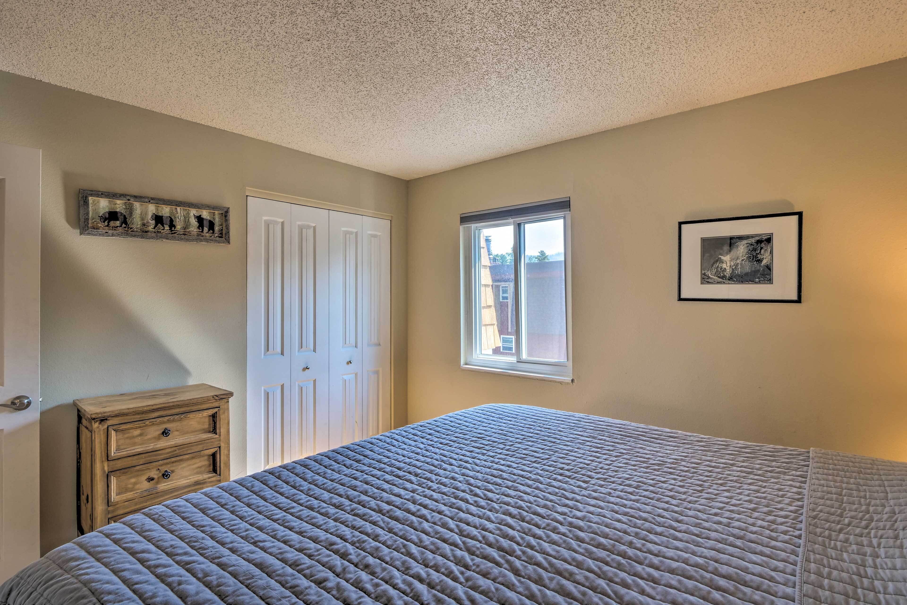 A bedroom with a large bed, a dresser, a closet, a window, and a framed picture on the wall.