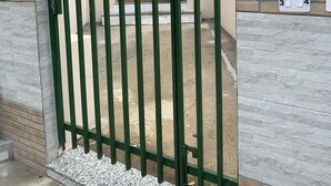 Una entrada protegida con muro de ladrillo y base de piedra, que conduce a una puerta de madera.