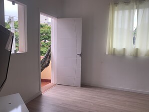 A room with a white door, a small window, and a view of greenery outside.