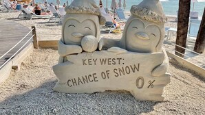 En strandscen med en sandskulptur som föreställer två snögubbar och en skylt med texten: "Key West: Sannolikhet för snö 0 %".