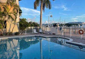 A swimming pool with a clear view of the surrounding area, including a building with balconies and palm trees.