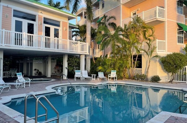 A pool area with lounge chairs and a building with balconies.