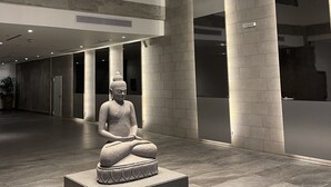 Ein modernes Interieur mit einer großen Buddha-Statue auf einem Sockel, einer hohen Decke mit einer besonderen Leuchte und einem großzügigen Grundriss mit hohen Säulen.