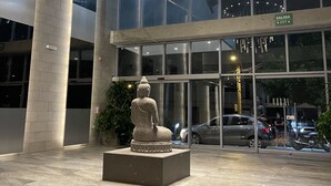 Ein moderner Gebäudeeingang mit Buddha-Statue, Glasfassade und einer runden Leuchte.