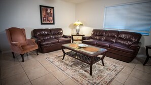 A living room with two brown leather sofas, a brown armchair, a glass coffee table, a patterned rug, a lamp, and a framed picture on the wall. - Close to Attractions, Sleeps 4 (Orlando)