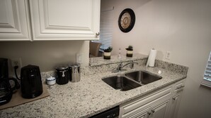 A kitchen with white cabinets, a granite countertop, a stainless steel sink, and a clock on the wall. - Close to Attractions, Sleeps 4 (Orlando)