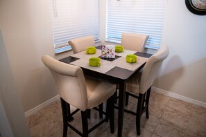 A dining table with four chairs, a decorative placemat, and a clock on the wall.