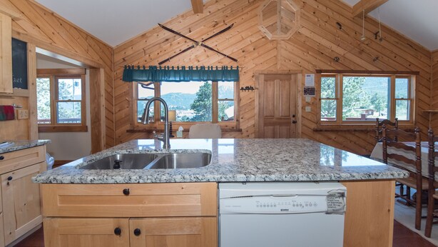 A kitchen with wooden walls, a granite countertop, a built-in dishwasher, and a window overlooking a mountainous landscape. - Perfect Mountain Home II with HOT TUB overlooking Mary's Lake/Near RMNP entrance (Estes Park)