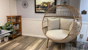 A room with a round wicker chair with cushions, a wooden bookshelf, and a potted plant. - Your Comfy Home in Pittsburgh with King beds and free parking (Pittsburgh)