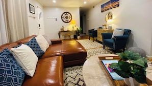 A modern living room with a brown leather sofa, a blue armchair, a coffee table, and a ceiling fan. - Your Comfy Home in Pittsburgh with King beds and free parking (Pittsburgh)