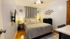 A bedroom with a bed, bedside tables, a ceiling fan, a wall-mounted TV, and a door. - Your Comfy Home in Pittsburgh with King beds and free parking (Pittsburgh)