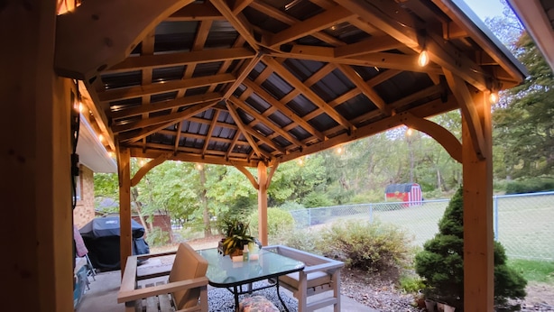 A covered patio area with a table and chairs, a grill, and a view of the surrounding greenery. - Your Comfy Home in Pittsburgh with King beds and free parking (Pittsburgh)