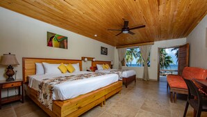 A room with two wooden beds, a wooden ceiling fan, a wooden table, and a view of the ocean. - Pelican Beach Resort (Dangriga)