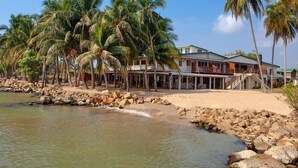 A beachfront property with a large house, palm trees, and a rocky shoreline. - Pelican Beach Resort (Dangriga)