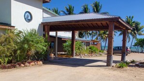A covered outdoor area with a building in the background, palm trees, and a clear sky. - Pelican Beach Resort (Dangriga)