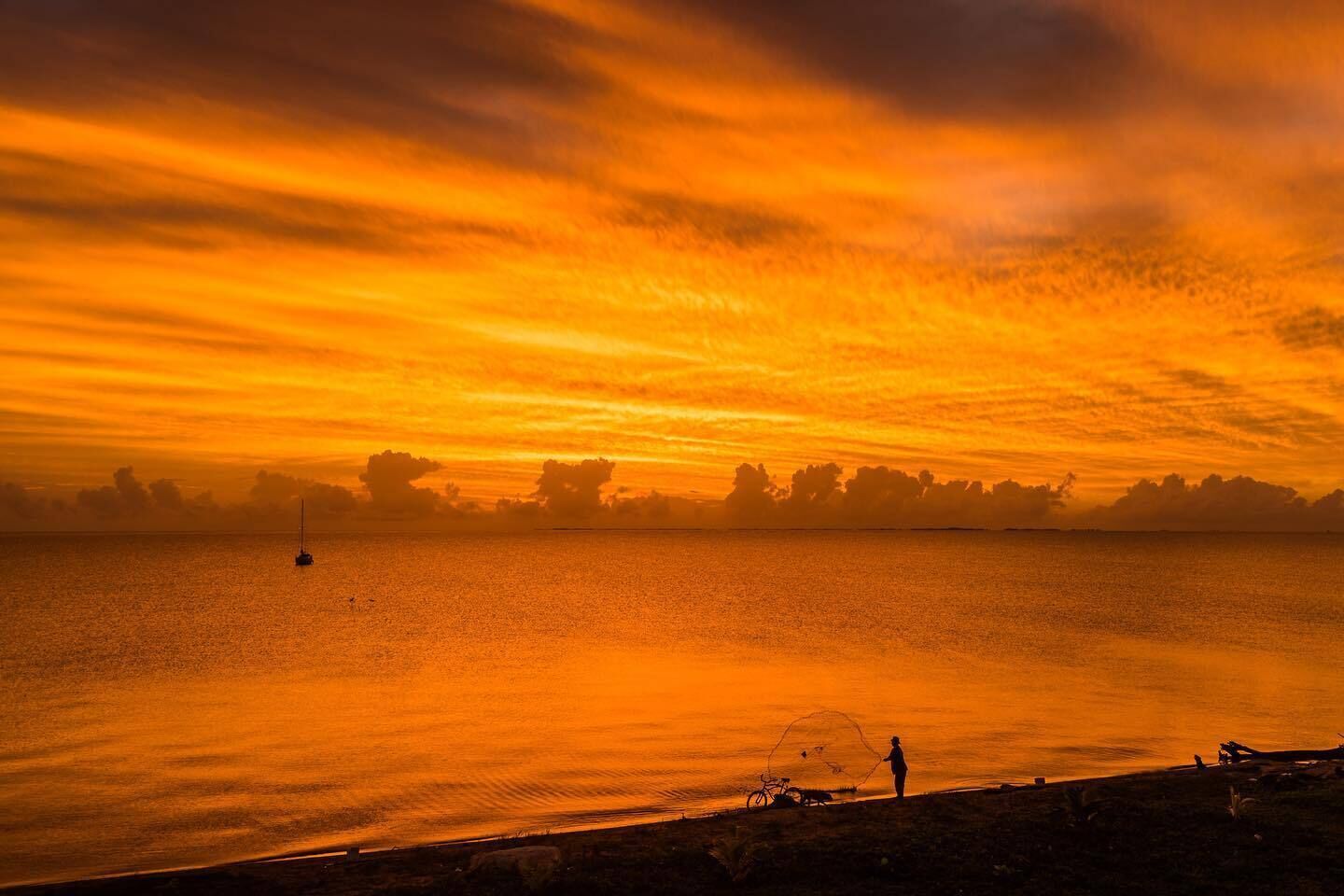 Een zonsondergang boven een kalm wateroppervlak, met een verafgelegen silhouet van de kustlijn.